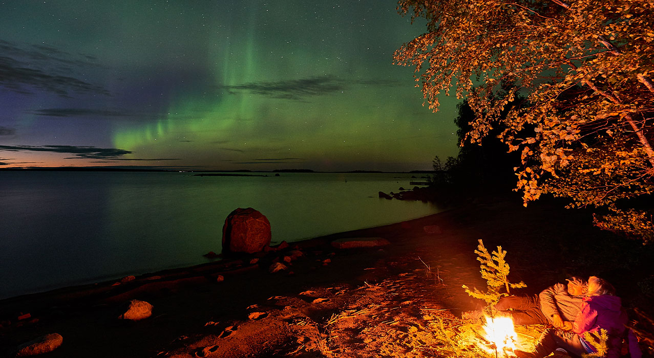 Paar am Feuer bei der Nordlichterbeobachtung in Schwedisch Lappland - Brändön Lodge Graeme Richardson